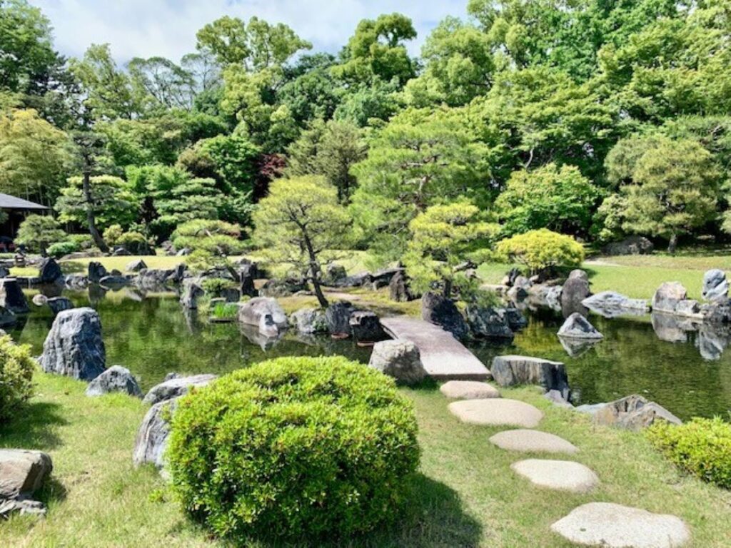 Traditional Japanese zen garden with stone stepping path crossing pond surrounded by manicured trees and rocks