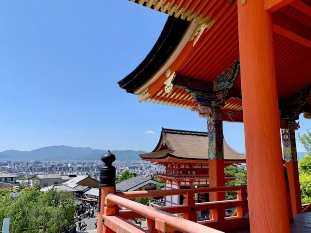 Red vermillion temple balcony overlooking Kyoto cityscape with traditional pagoda rooftops and distant mountains