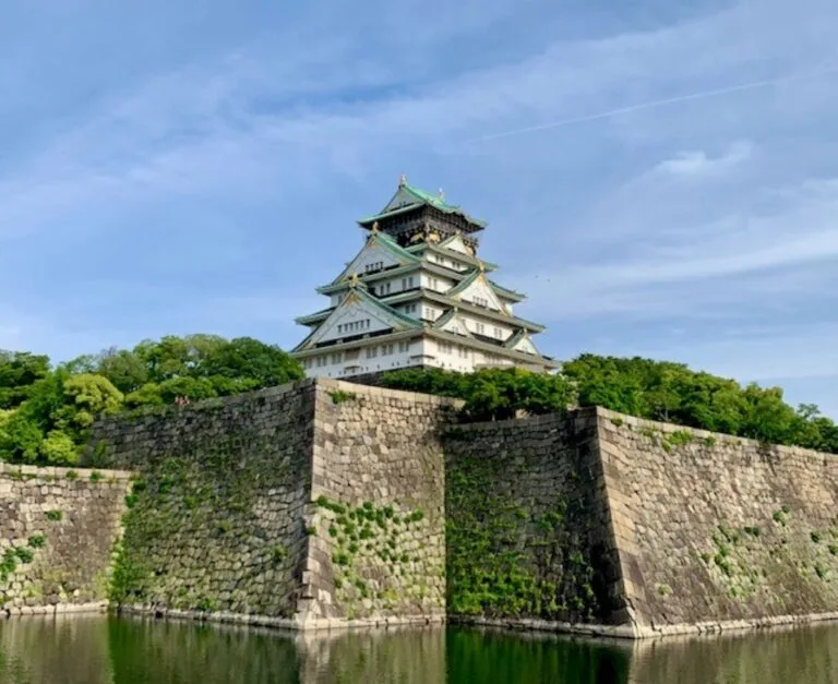 Osaka Castle's white stone walls and green-roofed keep rising above defensive moat on a clear day
