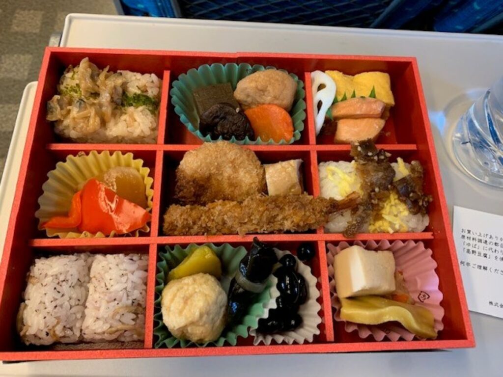 Traditional Japanese bento box with nine compartments containing rice, fish, vegetables and pickles