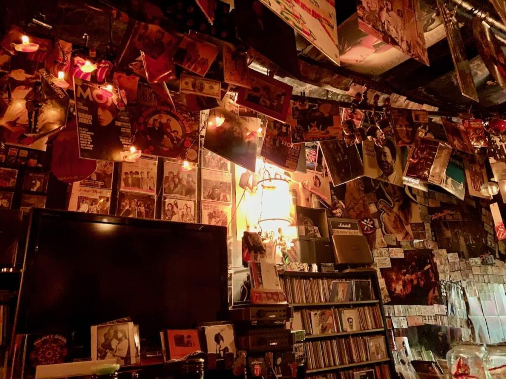 Dimly lit interior of Fanny Mae's bar in Osaka, walls and ceiling covered in vinyl records, Rolling Stones posters and rock memorabilia