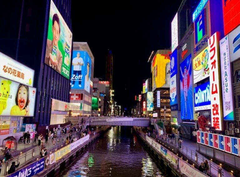 Glico running man by the canal in Dotonburi surrounded by neon signs and people walking