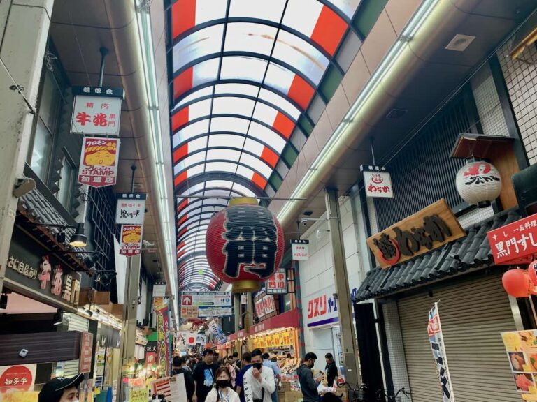 Covered arcade of Kuromon Ichiba Market in Osaka, big red lantern overhead, food stalls and shop signs lining the busy walkway