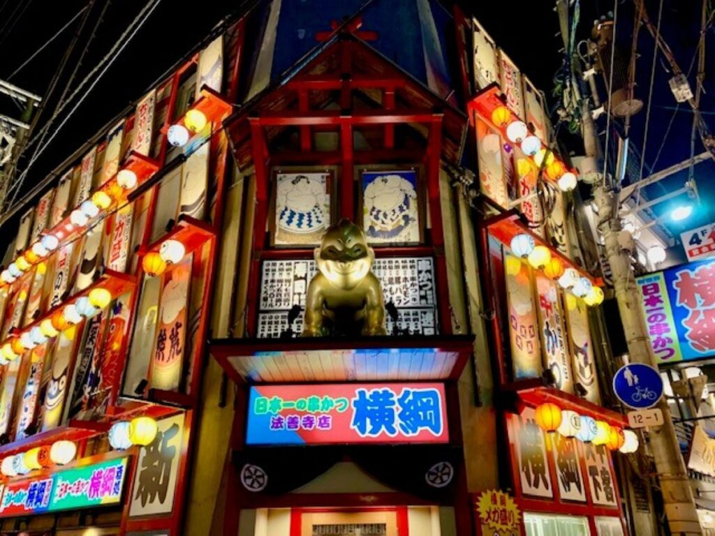 Kushikatsu restaurant facade in Shinsekai, Osaka, lit with lanterns and sumo-themed signs at night.