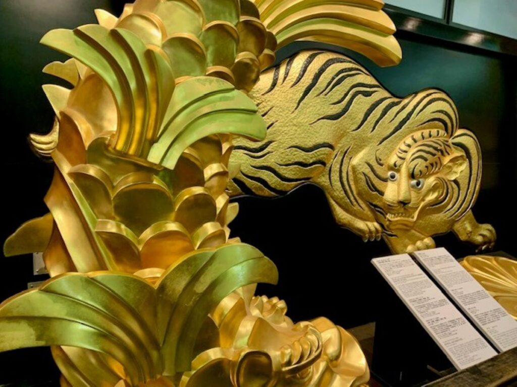 Gold shachihoko ornament and tiger relief on display inside Osaka Castle Museum, close-up detail.