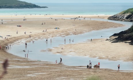 Crantock beach in cornwall at low tide. The beach is full with people exploring the sand and rock pools