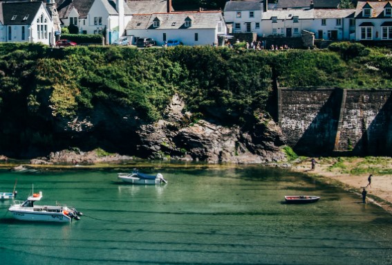 Port Isaac bay in Cornwall. Boats sit on top of the turquoise water with the village perched on the cliff above