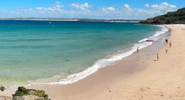 Porthminster Beach St Ives with turquoise waters and waves lapping the golden sand shore as people play in the water