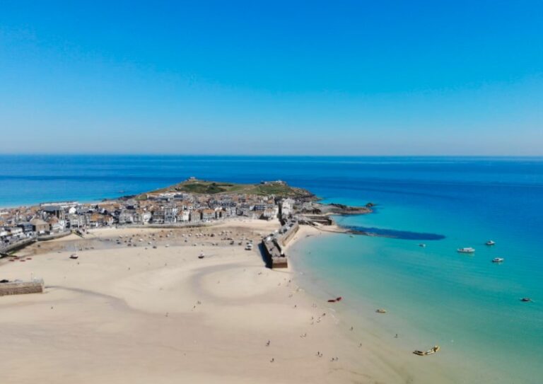 St Ives at low tide with a vase expanse of sand and turquoise water. Dotted with people playing and boats in the water