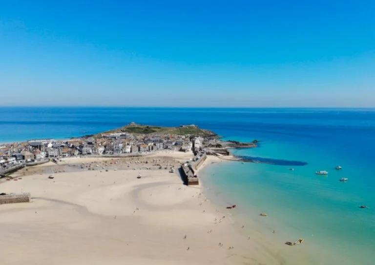 St Ives at low tide with a vase expanse of sand and turquoise water. Dotted with people playing and boats in the water