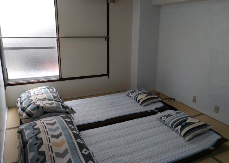 Traditional Japanese room with tatami flooring and two futon beds laid out. Geometric patterned bedding and frosted window.
