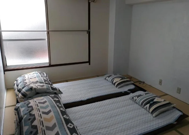 Traditional Japanese room with tatami flooring and two futon beds laid out. Geometric patterned bedding and frosted window.