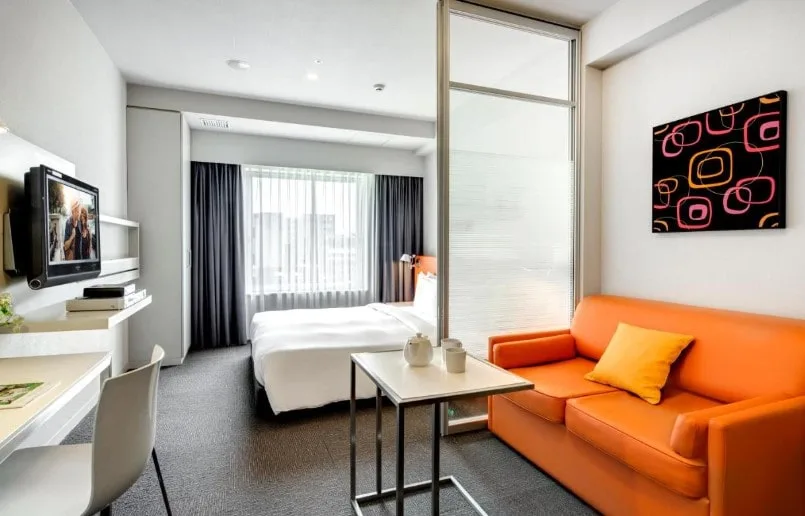 Spacious double room with orange sofa and seating area at Citadines Shinjuku Tokyo