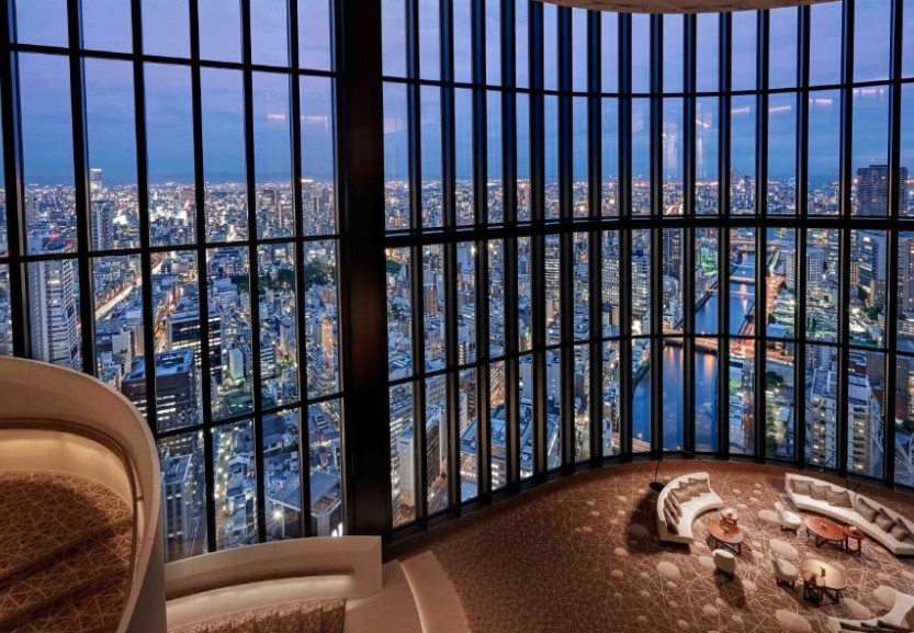 Curved observation lounge with floor-to-ceiling windows showcasing Osaka's night skyline. Curved seating area with cushioned benches