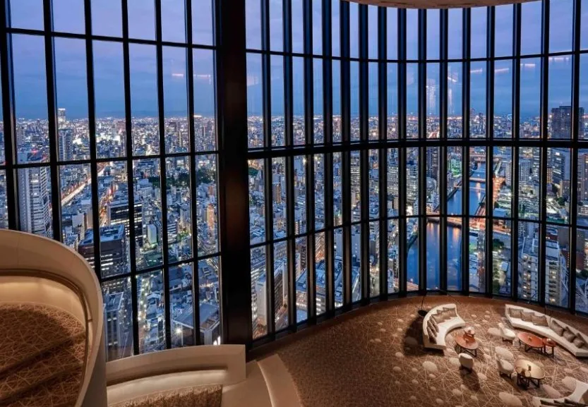 Curved observation lounge with floor-to-ceiling windows showcasing Osaka's night skyline. Curved seating area with cushioned benches