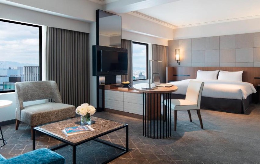 Deluxe room with marble coffee table, rotating TV stand and city views. Features grey lounge chair and wooden desk area