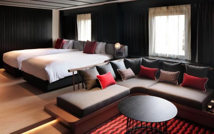 Spacious twin room with black panelled walls, large L-shaped sofa with red cushions, and black coffee table on red rug