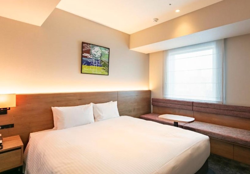 Double hotel room with wooden headboard, wall-mounted TV, built-in window bench, and ambient lighting