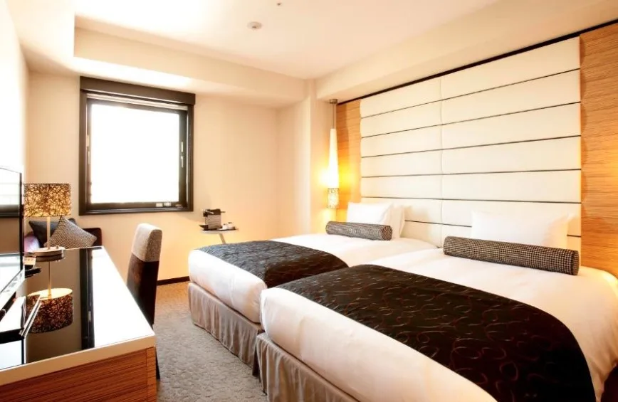 Modern twin room with wooden furnishings, black and white bedding, geometric headboard panel and desk area near window.