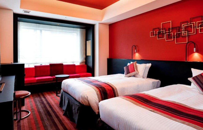 Twin room with bold red walls, geometric art, window seating area and striped bed runners in red and black