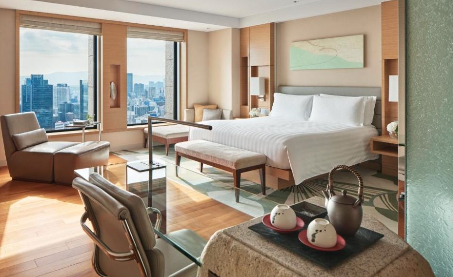 Modern hotel room with panoramic city views, king bed, tea service and contemporary furnishings in warm wood tones