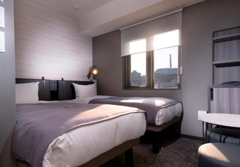 Contemporary twin room with city views through window, grey bedding, and minimalist décor in neutral tones