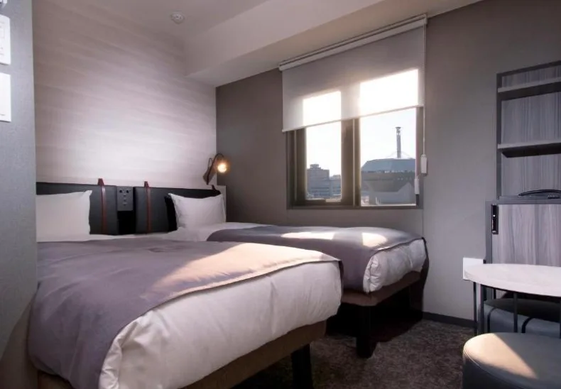 Contemporary twin room with city views through window, grey bedding, and minimalist décor in neutral tones