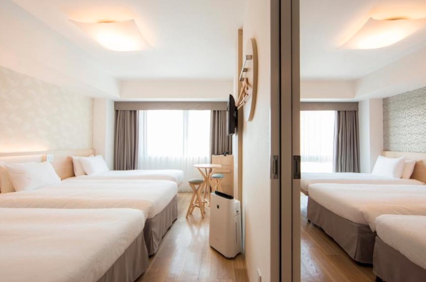Bright twin room with mirrored wall, wooden side tables and grey bed skirts, featuring air purifier and modern ceiling lights