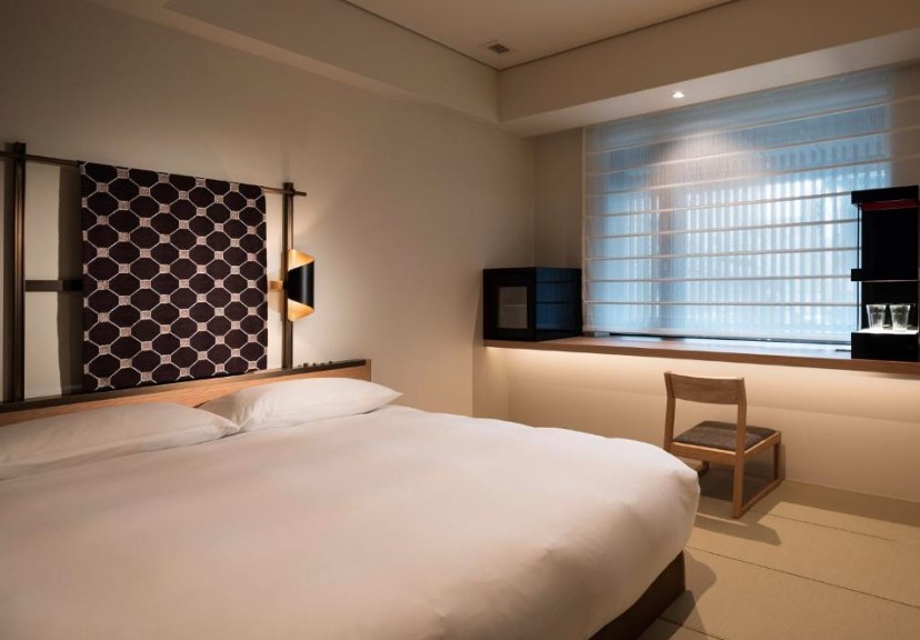 Modern Japanese bedroom with geometric fabric headboard, double bed and wooden floor seat. Contemporary lighting and blinds.