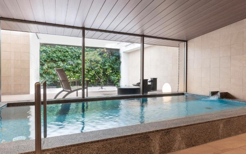 Indoor pool with glass wall overlooking zen garden, featuring stone surround and modern loungers