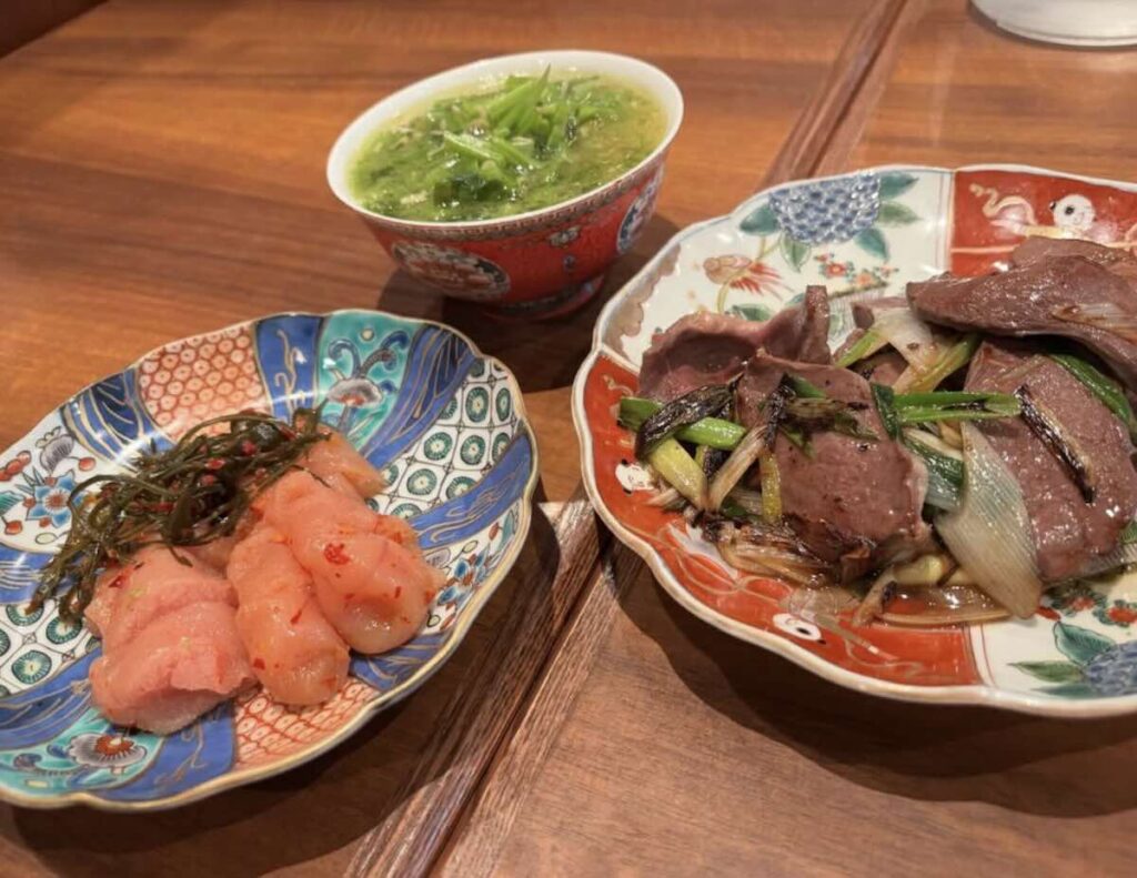 Three dishes on patterned ceramics: marinated cod roe with seaweed, sautéed liver with leeks, and a green vegetable soup.