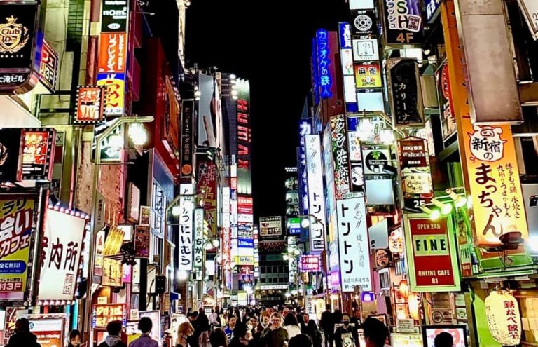 Vibrant night scene in Shibuya with brightly lit signs and billboards, and crowds of people walking through the bustling streets