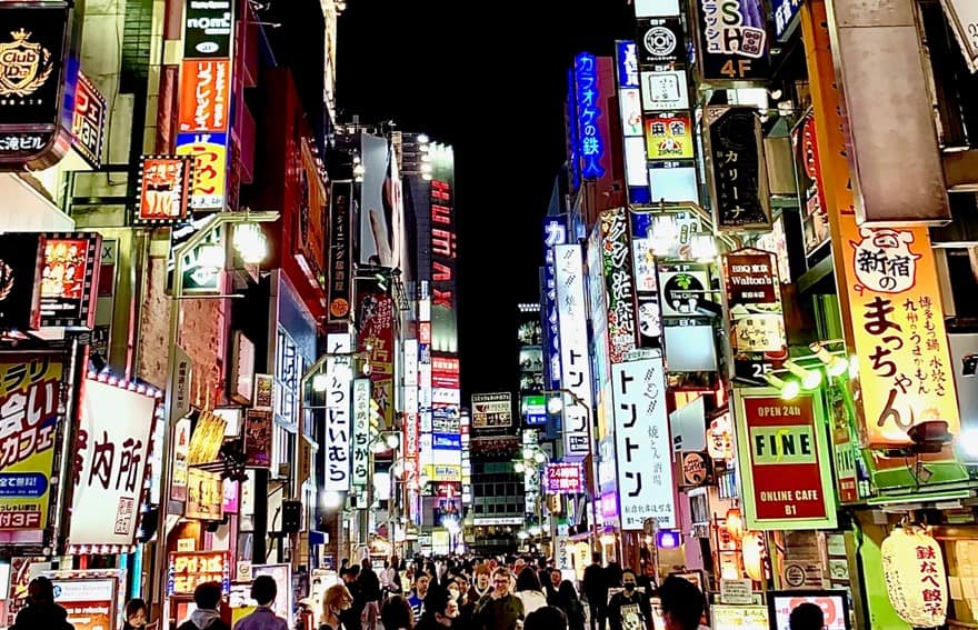 Vibrant night scene in Shibuya with brightly lit signs and billboards, and crowds of people walking through the bustling streets