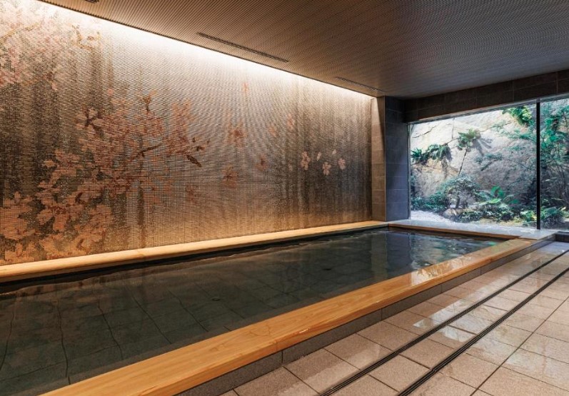 Indoor onsen bath with cherry blossom wall mural and garden view