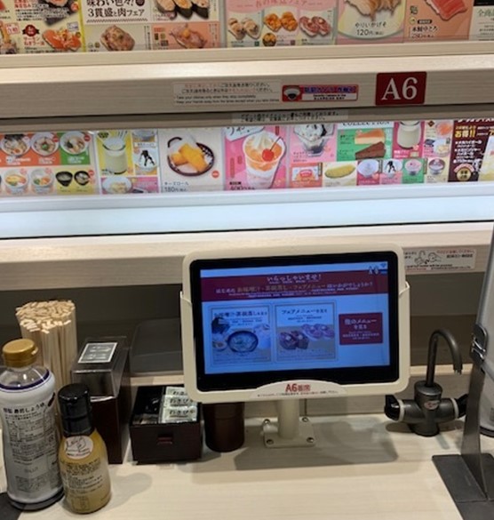 Interactive touchscreen menu at Uobei robotic sushi restaurant in Tokyo, displaying various sushi options and condiments like soy sauce and chopsticks on the counter