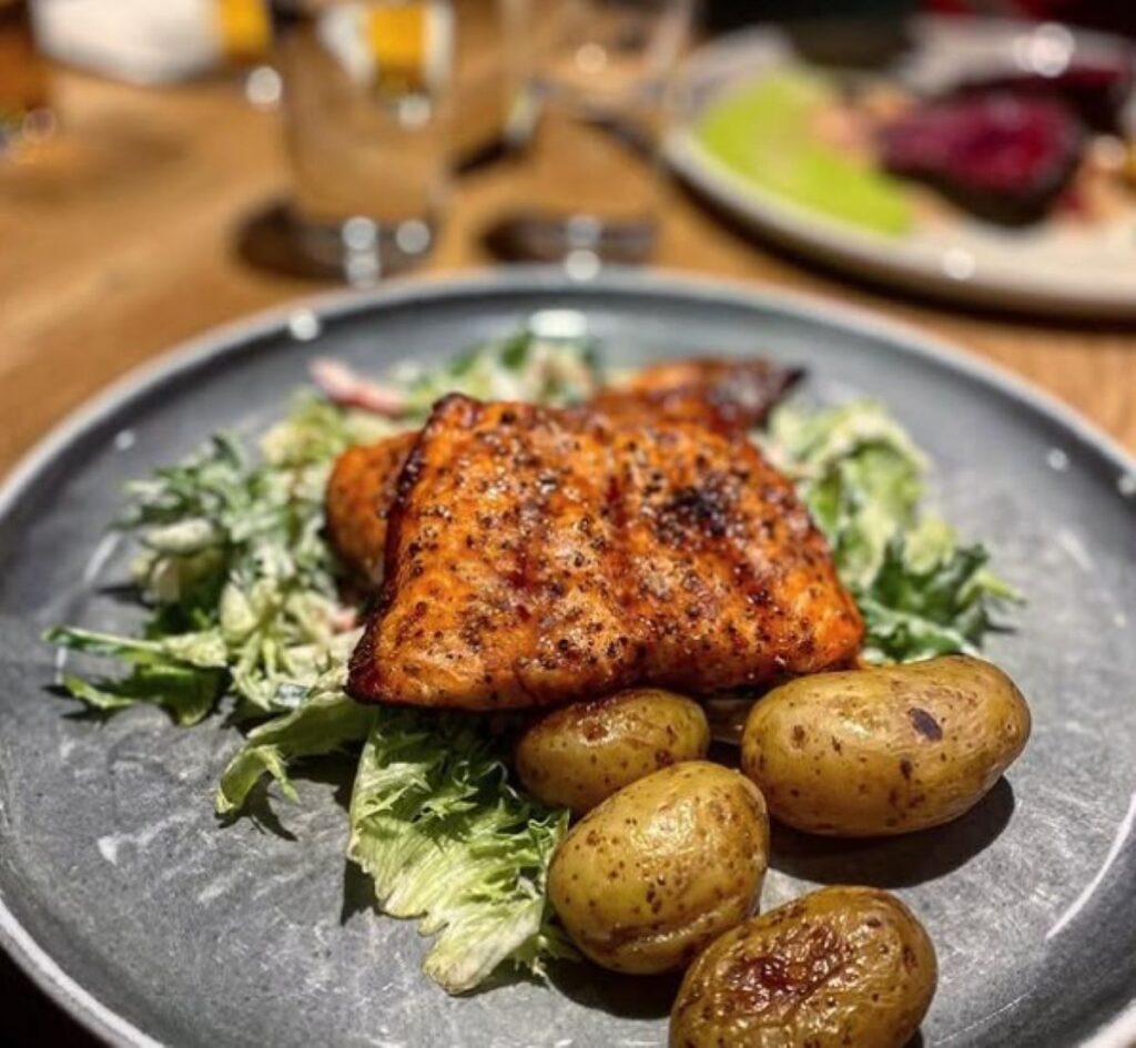 Pan-seared salmon fillet with baby potatoes and fresh salad leaves on grey plate, showcasing local Arctic fish preparation