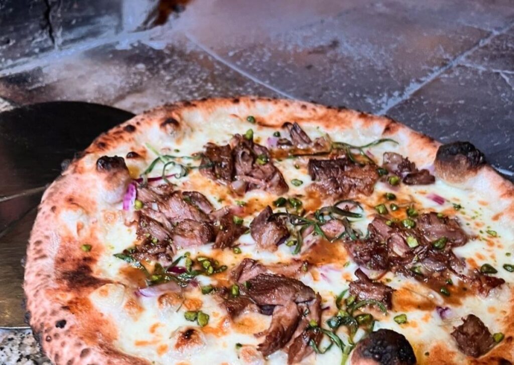 Wood-fired pizza topped with sliced beef, wild mushrooms, caramelised onions and fresh herbs on charred sourdough base