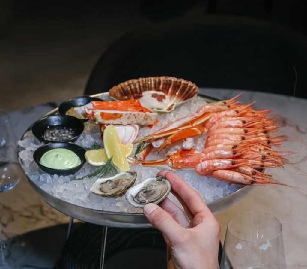 Fresh seafood platter with king crab, prawns, scallop and oysters on ice, Arctic shellfish display with green dipping sauce