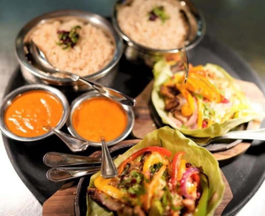 Indian curry platter with orange dal, pilau rice, naan bread and colourful vegetable dishes served in traditional metal bowls
