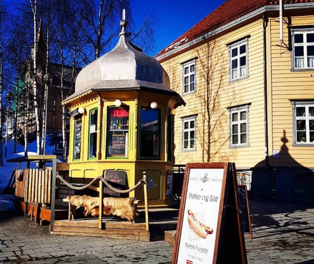 Traditional Norwegian pølse og øl kiosk with yellow wooden exterior and dome roof advertising sausages and beer