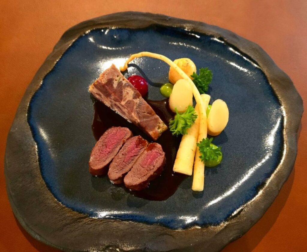 Sliced beef with white asparagus, berry compote and dark sauce on blue ceramic plate, fine dining presentation on wooden table