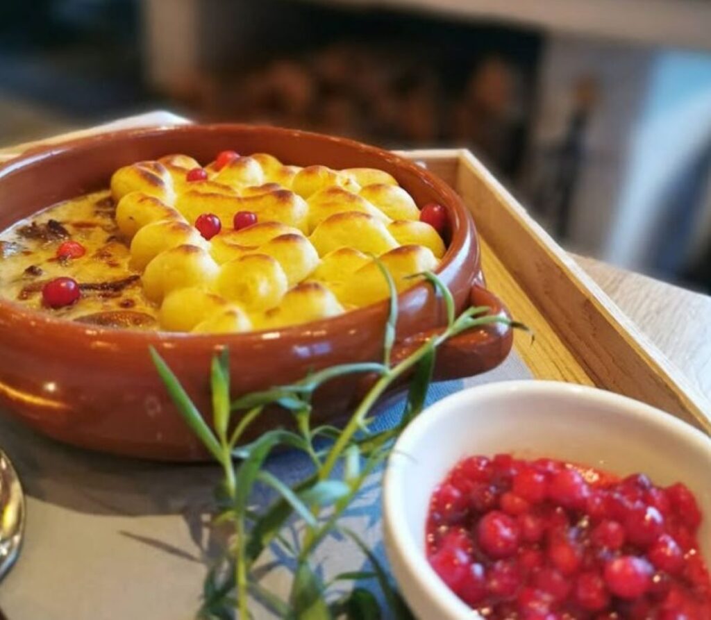 Golden potato gratin with lingonberry sauce in traditional terracotta dish, classic Scandinavian comfort food with fresh herbs