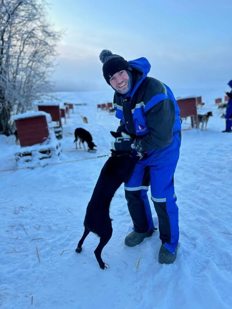 A heartwarming scene in Tromsø, Norway, featuring a cheerful encounter with a playful sled dog amidst a snowy landscape and serene blue skies.