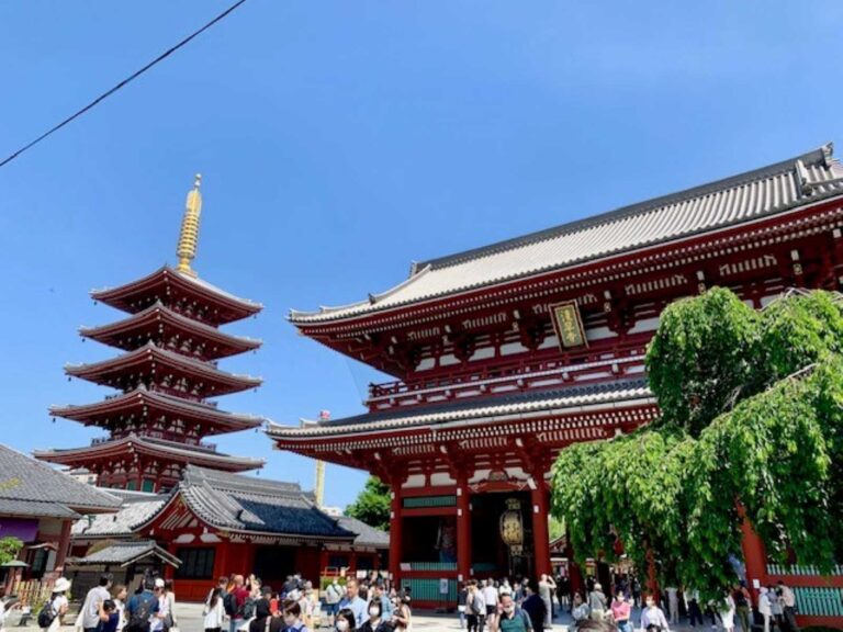 This image captures the Sensoji Temple, one of the most famous historical landmarks in Tokyo's Asakusa district. The temple's iconic red pagoda and intricate architectural elements, including the curved rooflines and decorative wall patterns, are prominently featured. A number of people can be seen exploring the temple grounds, indicating the site's continued cultural significance and popularity among visitors