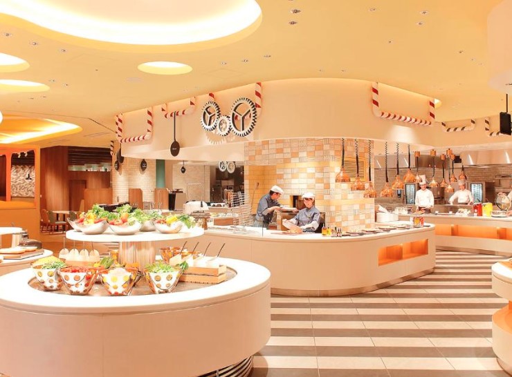 Modern hotel buffet restaurant with curved serving stations. Warm lighting and industrial-style ceiling decor with striped floor