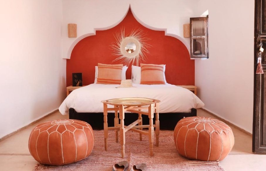 Riad bedroom with terracotta arched alcove, white bedding, leather poufs and brass tray table"