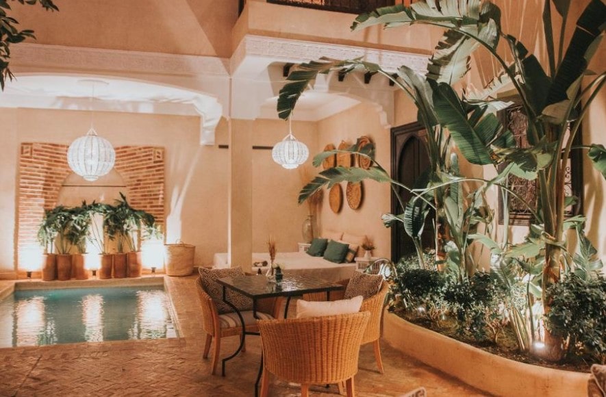 Riad courtyard with indoor pool, wicker dining furniture and tropical plants beneath white pendant lights