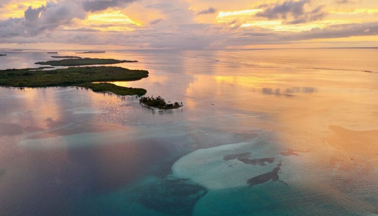 Aerial view of San Blas Islands: lush green islands and turquoise waters under golden sunset skies.