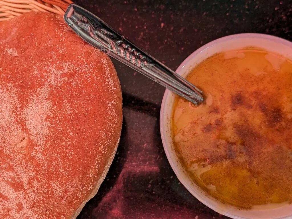 Crème brûlée in a white dish beside a sugared pastry, with an ornate spoon on a dark background.
