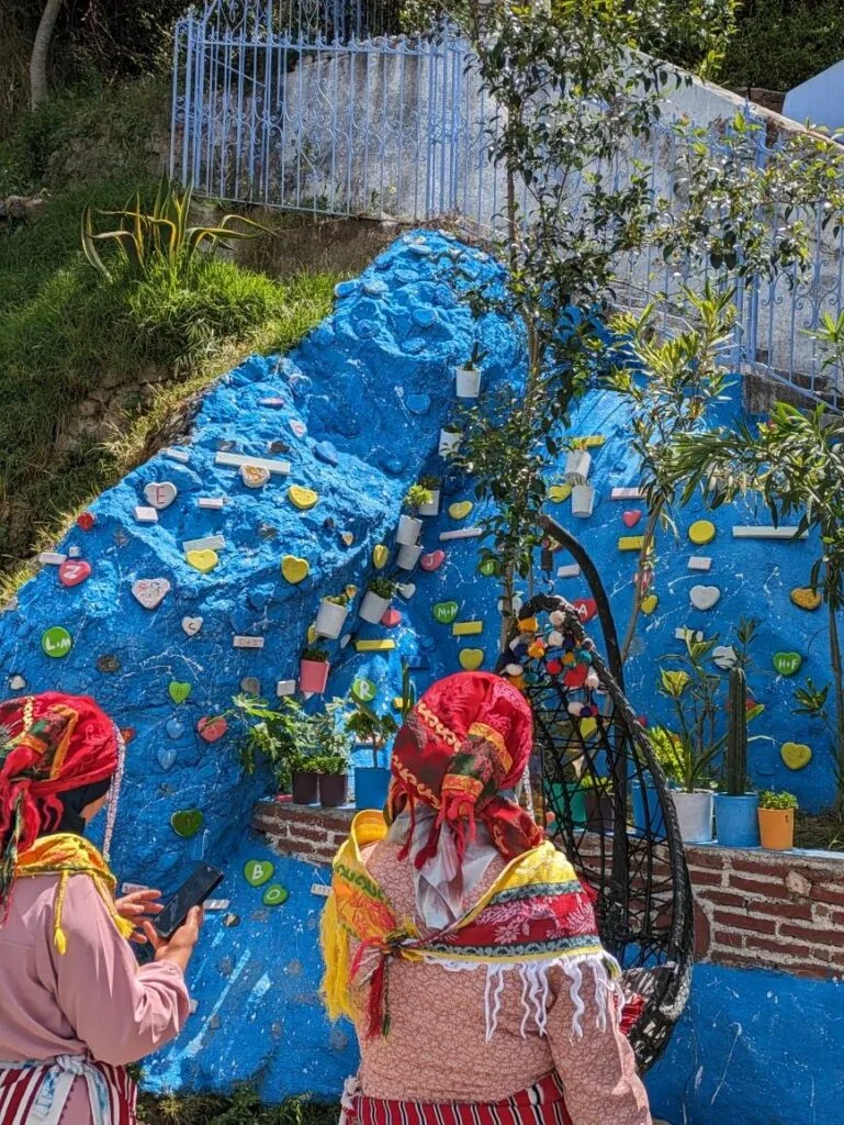 Blue painted wall with colourful heart-shaped decorations, two people in traditional dress observing.